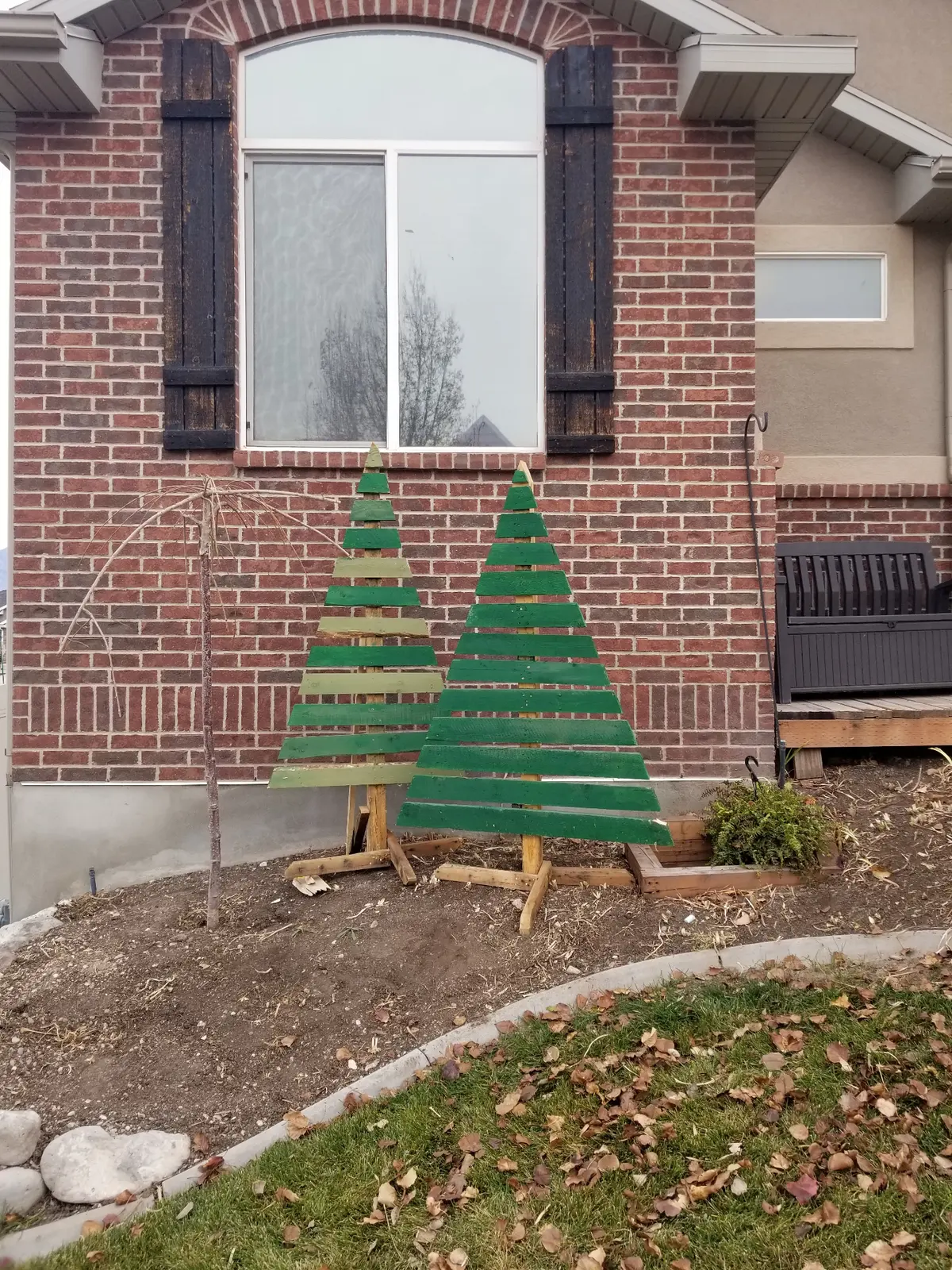 Two completed pallet Christmas trees with green paint displayed in front yard