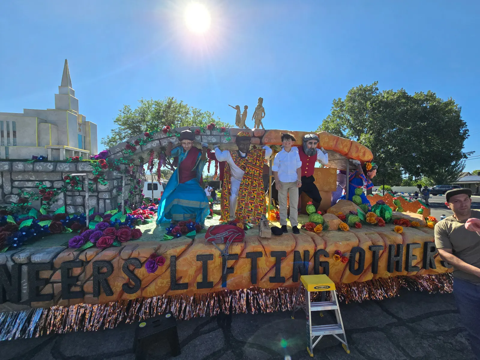 Completed parade float with decorations, flowers, and 'Vers Lifting Others' message