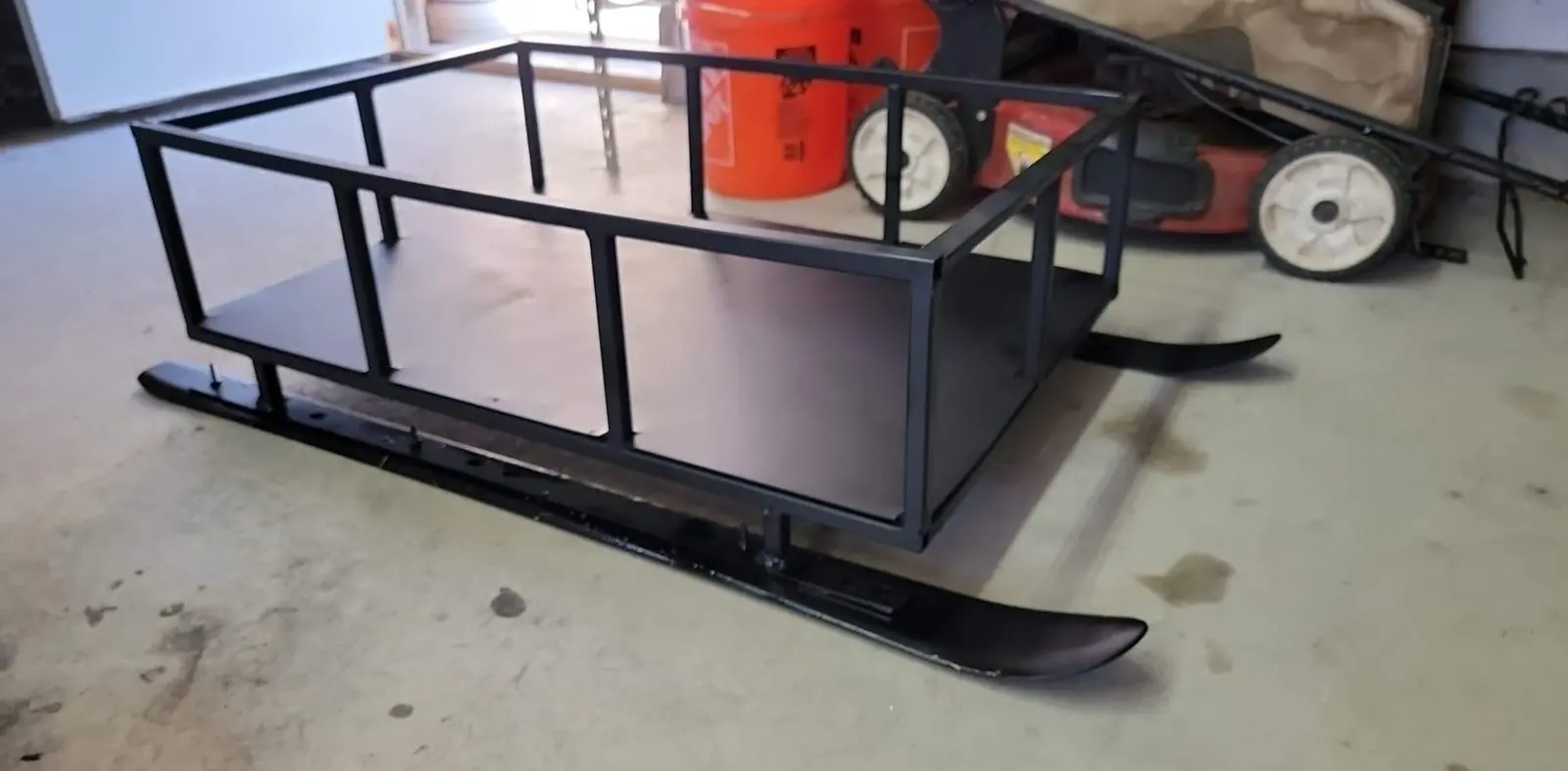 Snowmobile sled with welded steel frame and ski runners in garage