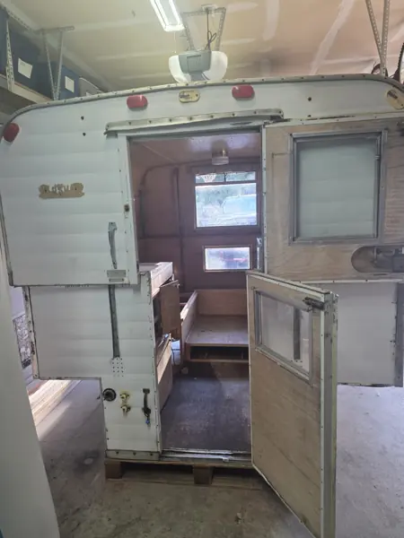Rear entrance of the Alaskan camper before restoration, looking through the open door into the unfinished interior
