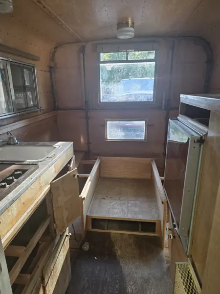 Original Alaskan camper interior viewed down the aisle, with plywood walls, seating and galley