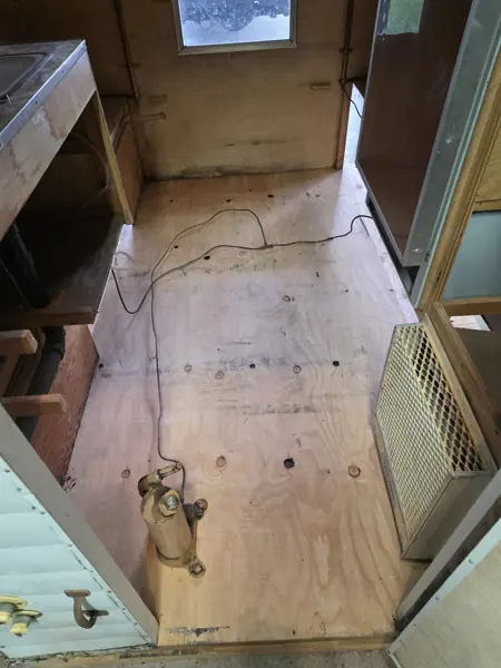 Camper aisle during work, with exposed plywood flooring and surrounding cabinets