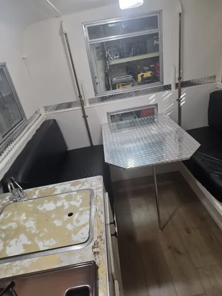 Finished camper dinette with black bench cushions, a metal-topped table and wood-look flooring