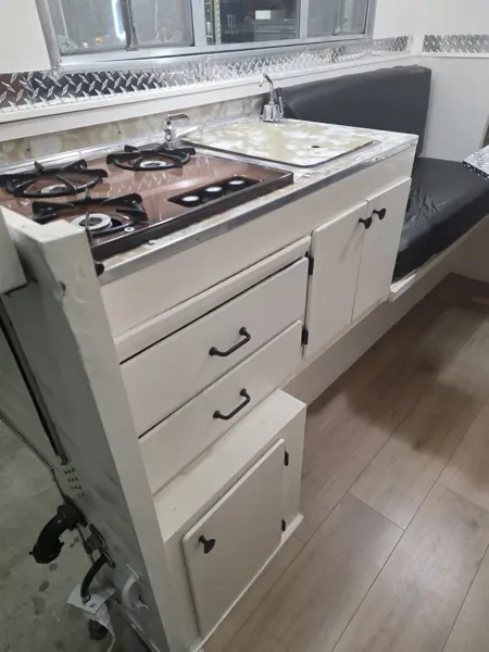 Refinished camper galley with white drawers and cabinet doors, cooktop, sink cover and black dinette cushion