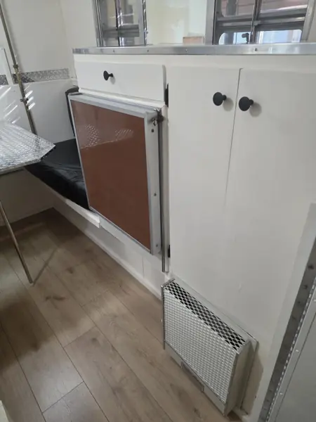 White camper storage cabinetry and refrigerator front beside the dinette and wood-look floor