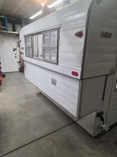White Alaskan camper exterior after restoration, with custom Alaskan Camper decals visible on the side and rear