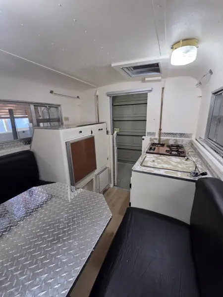 Wide reverse view inside the refinished camper, showing the dinette, white cabinets, sink and cooktop