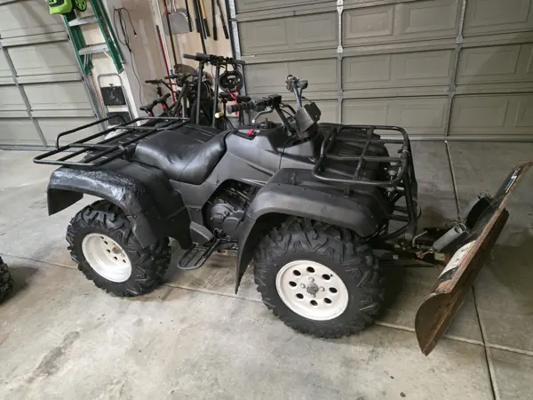 Reassembled ATV in a broad side view with dark body panels, seat, cargo racks and mounted snowplow