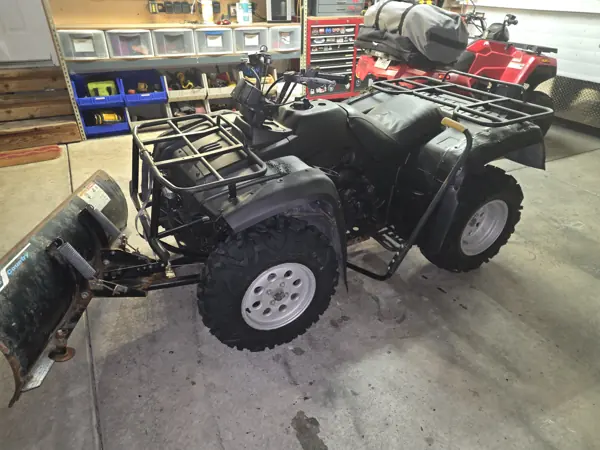 Opposite-side view of the reassembled ATV with dark bodywork, cargo racks and snowplow