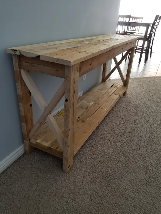 Unpainted console table with its wooden top, lower shelf and cross-braced ends in place.