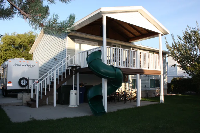 Covered raised deck with stairs, light-colored railings and a green spiral slide.