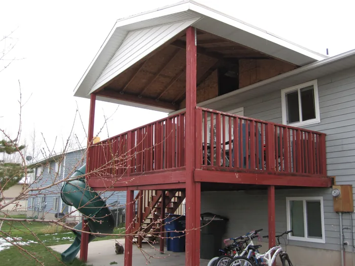 Angled view of the covered deck, stairs and spiral slide with red-finished railings.