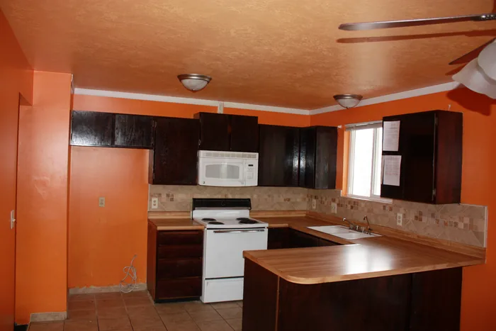 Kitchen before renovation, with dark cabinets, orange walls and a peninsula.