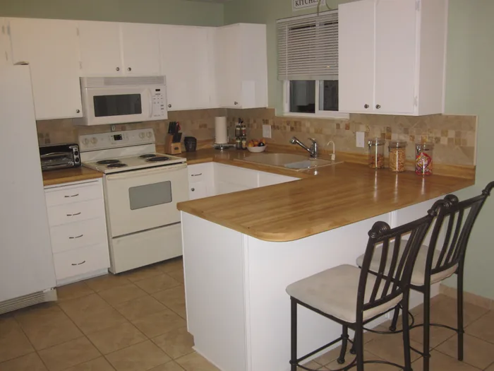 Finished kitchen with white cabinets, wood counters and a clear peninsula.
