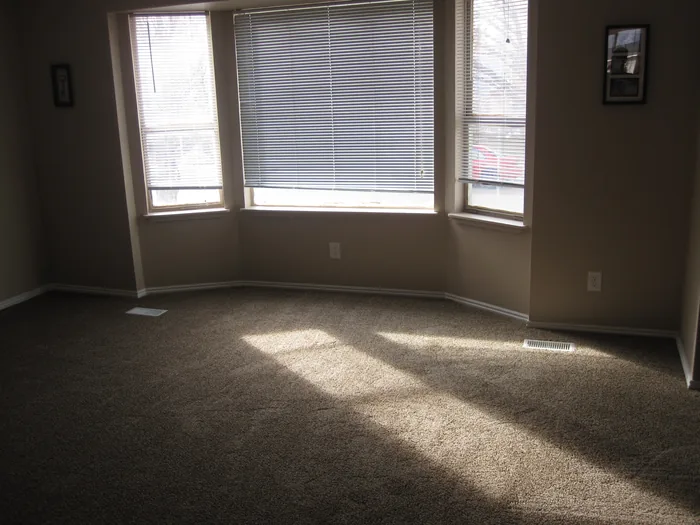 Finished living room with neutral walls and fresh carpet beside the bay window.
