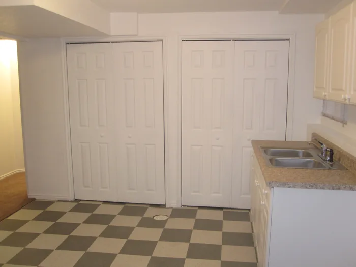 Finished basement kitchen with white cabinets, a sink and checkerboard flooring.