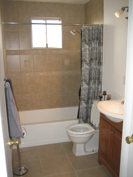 Completed bathroom with tiled tub surround, toilet and wood vanity.