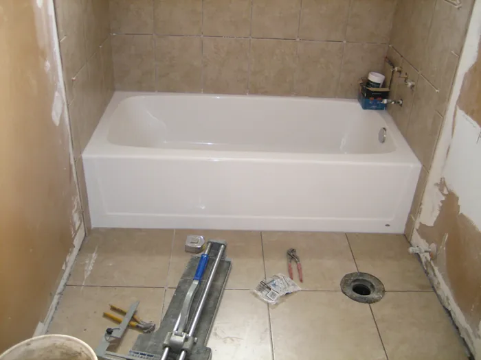 Tiled tub surround in place while tools and materials remain on the unfinished floor.