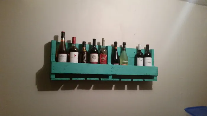 Green wall-mounted wooden wine rack holding bottles, with stemware slots underneath.