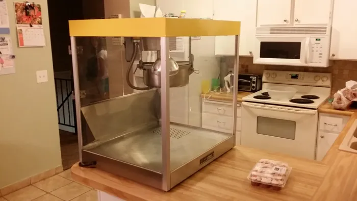 Cleaned popcorn machine on a kitchen counter, showing the yellow canopy, glass cabinet and kettle