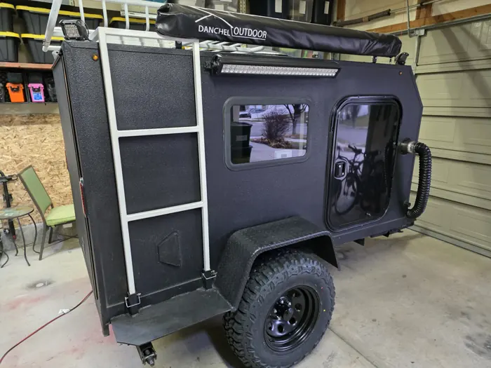 Rear three-quarter view showing the side window, ladder and roof-mounted awning.