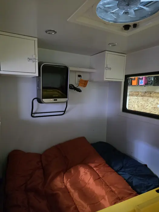 Sleeping cabin with overhead cabinets, a wall-mounted screen and roof vent.