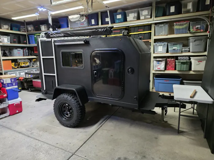 Square drop trailer with black wheels and a roof rack in the garage.